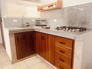 A kitchen with granite countertops, wooden cabinets, a gas stove, and a window with blinds.