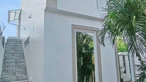 Un edificio moderno de dos pisos con fachada blanca, una ventana pequeña y una escalera visible que conduce a la entrada.