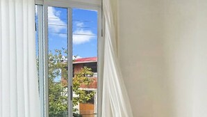 Una habitación de hotel con un amplio ventanal corredera que da a un balcón, una cama con cubierta acolchada y cortinas blancas.