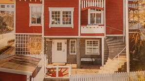 A red two-story house with a white picket fence, a flag, and a staircase leading to the entrance. - Smögen large rooms, on lovely Stenrös. (Västra Götalands län)
