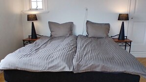 A bedroom with a large bed, two bedside tables, a window, and a door. - Smögen large rooms, on lovely Stenrös. (Västra Götalands län)