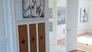 A spacious room with a large red patterned rug, a white wall with a colorful abstract painting, and a door leading to another room. - Smögen large rooms, on lovely Stenrös. (Västra Götalands län)