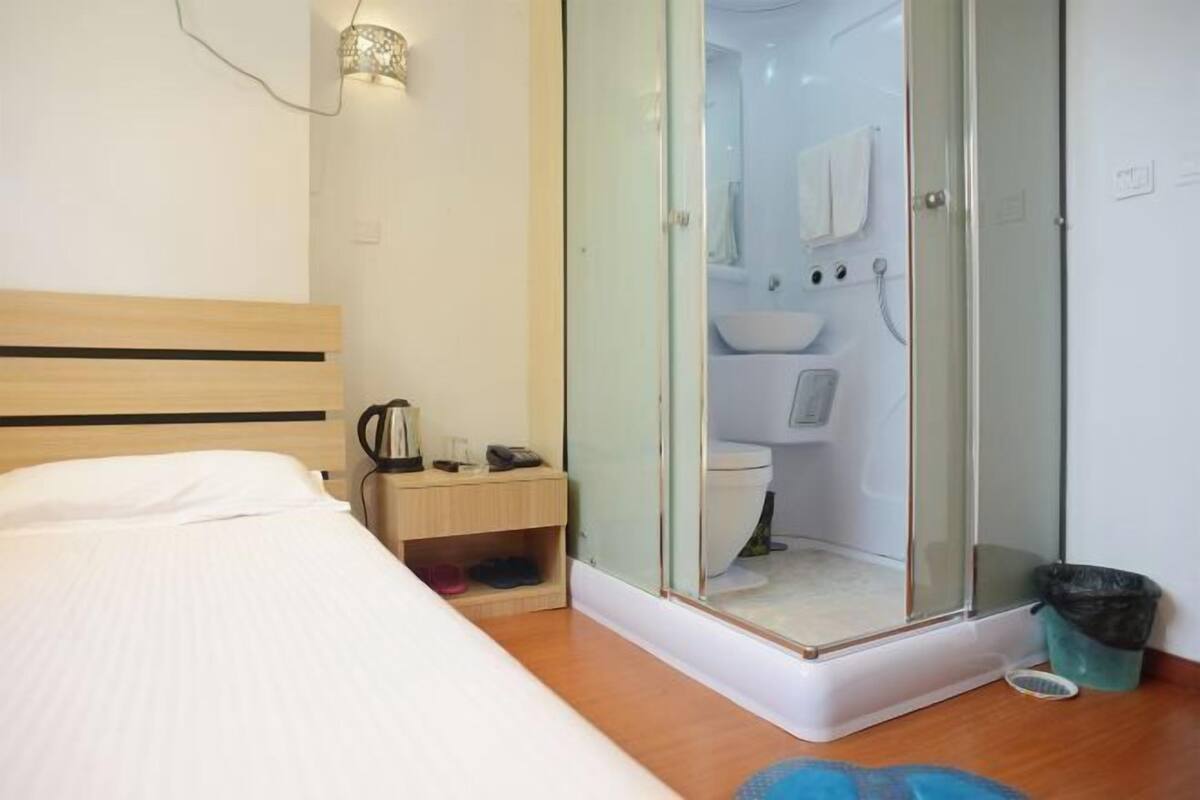 A bedroom with a bed, bedside table, and a glass-enclosed shower area with a toilet and sink.