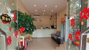A reception area with a desk, chairs, a potted plant, and a glass door with red signage.