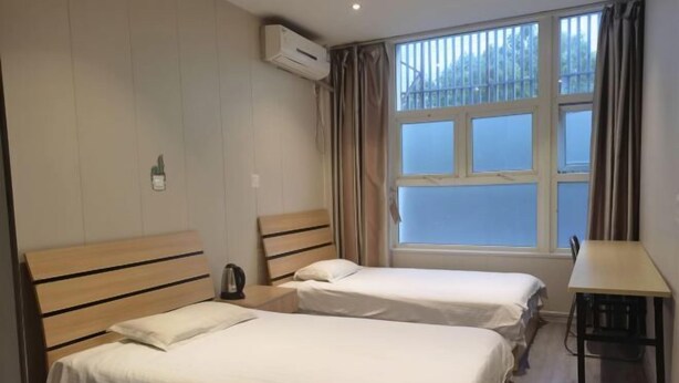 A room with two single beds, a wooden headboard, a small table, and a window with curtains.