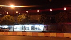 A building with illuminated signage, trees, and a car parked in front.