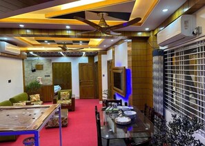 A hotel room with a dining area, a ceiling fan, and a large window with blinds. - Garden view villa  (Rajshahi)
