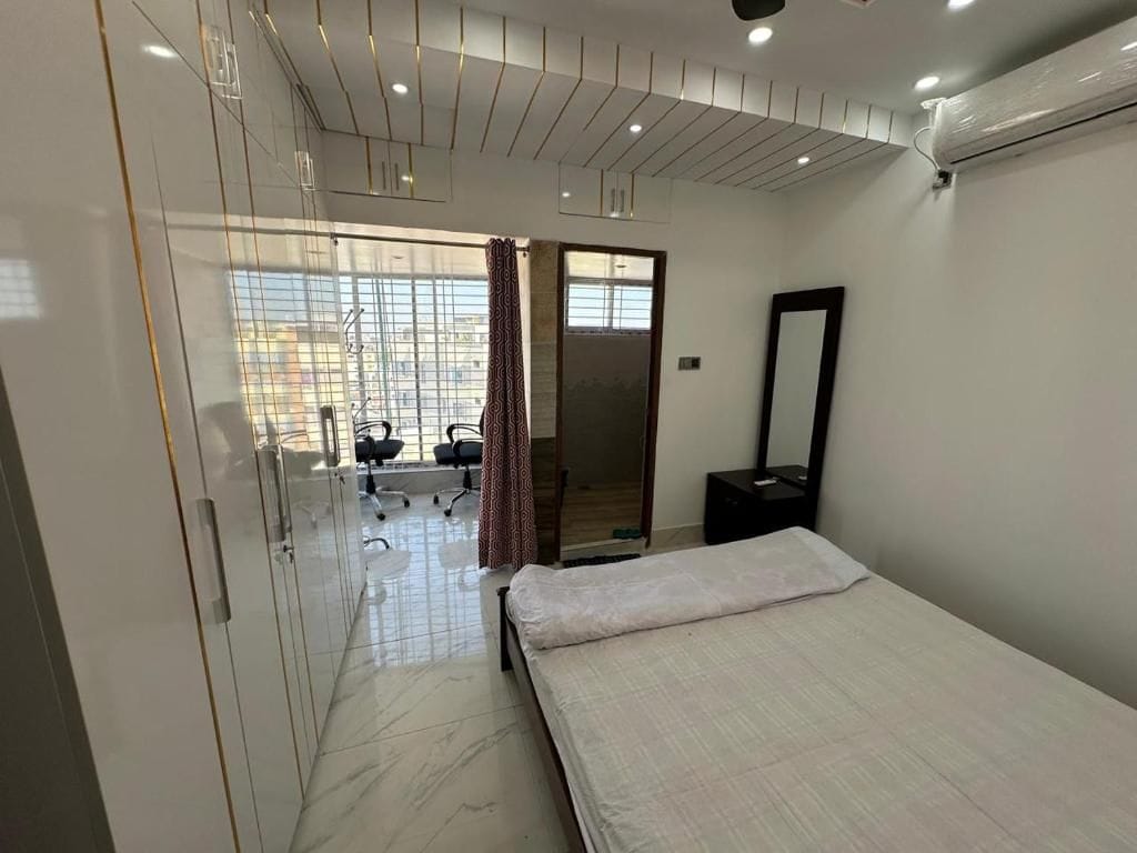 A hotel room with a bed, a desk, a chair, a mirror, and a view of the outside.