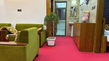 A hotel lobby with green sofas, a potted plant, a pink teddy bear decoration, and a red carpet.