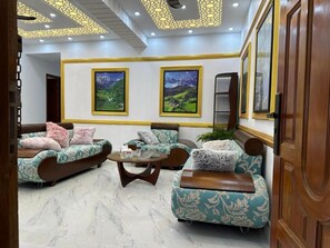 Un hall d’hôtel doté d’un espace détente comprenant des canapés et des fauteuils, une table basse et deux tableaux représentant des paysages, encadrés et accrochés au mur.