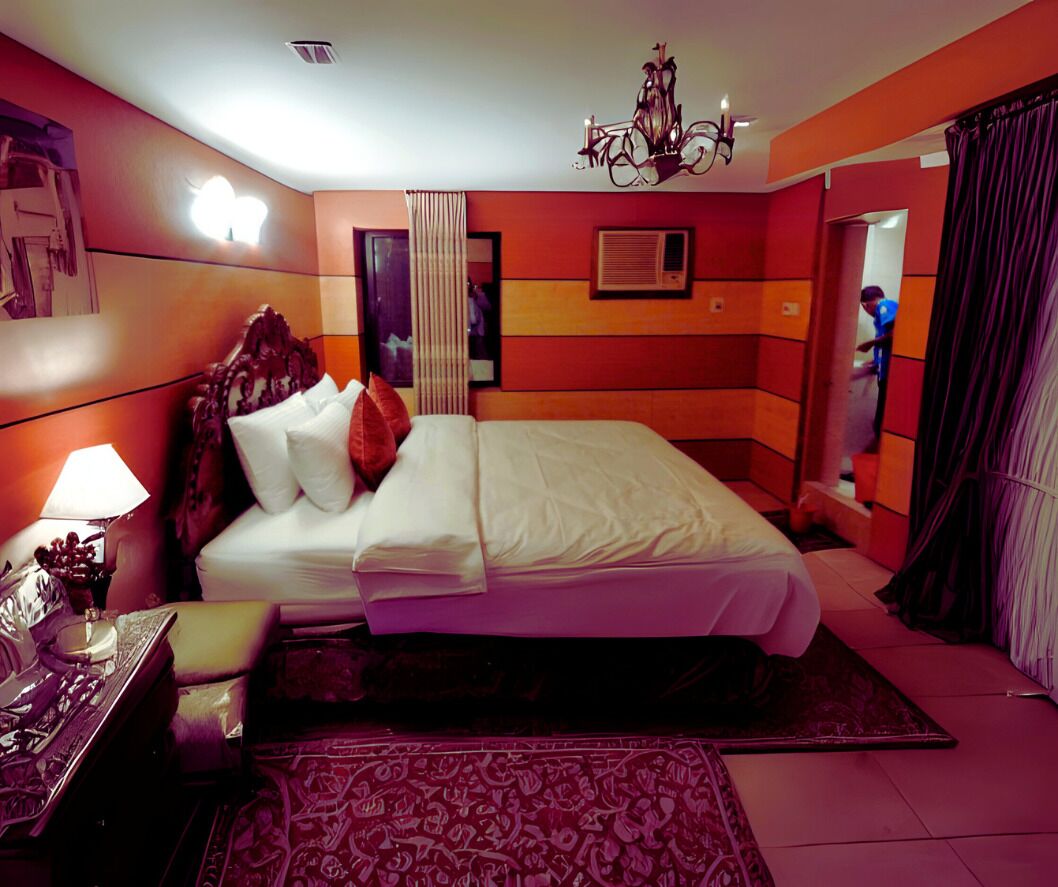 Habitación de hotel con una cama grande, un candelabro, una mesita de noche con lámpara y una alfombra estampada.