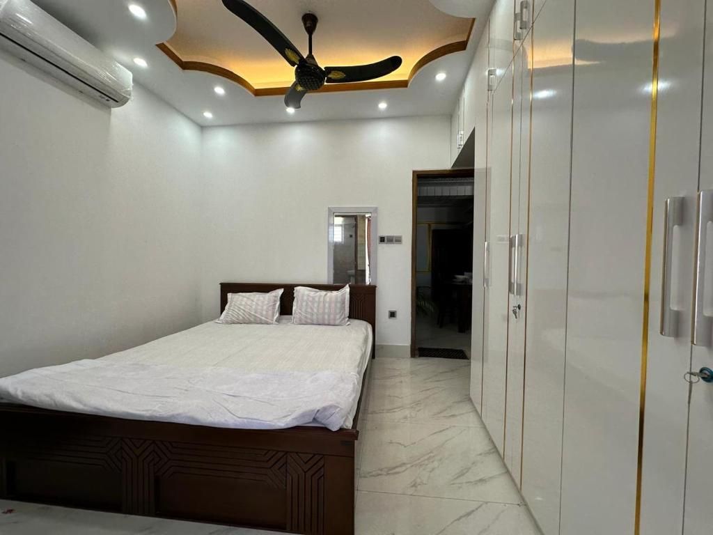 A bedroom with a bed, wardrobe, ceiling fan, and an air conditioning unit.