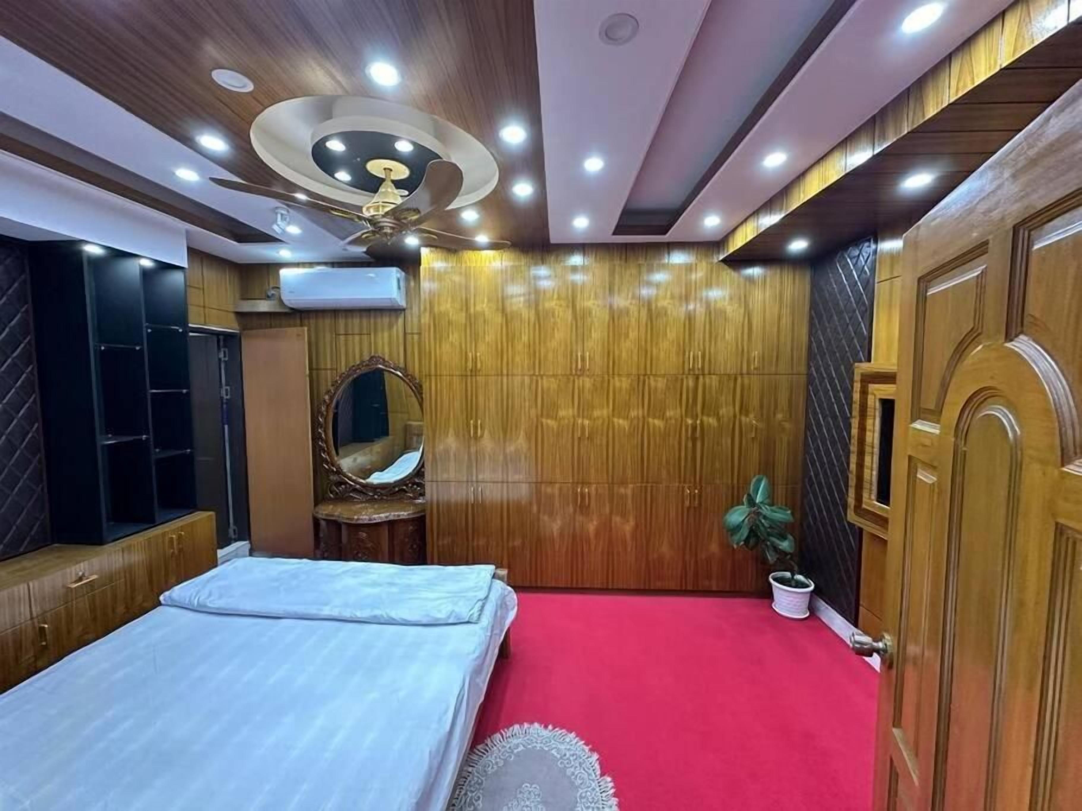 A bedroom with a bed, wardrobe, mirror, ceiling fan, and red carpet.