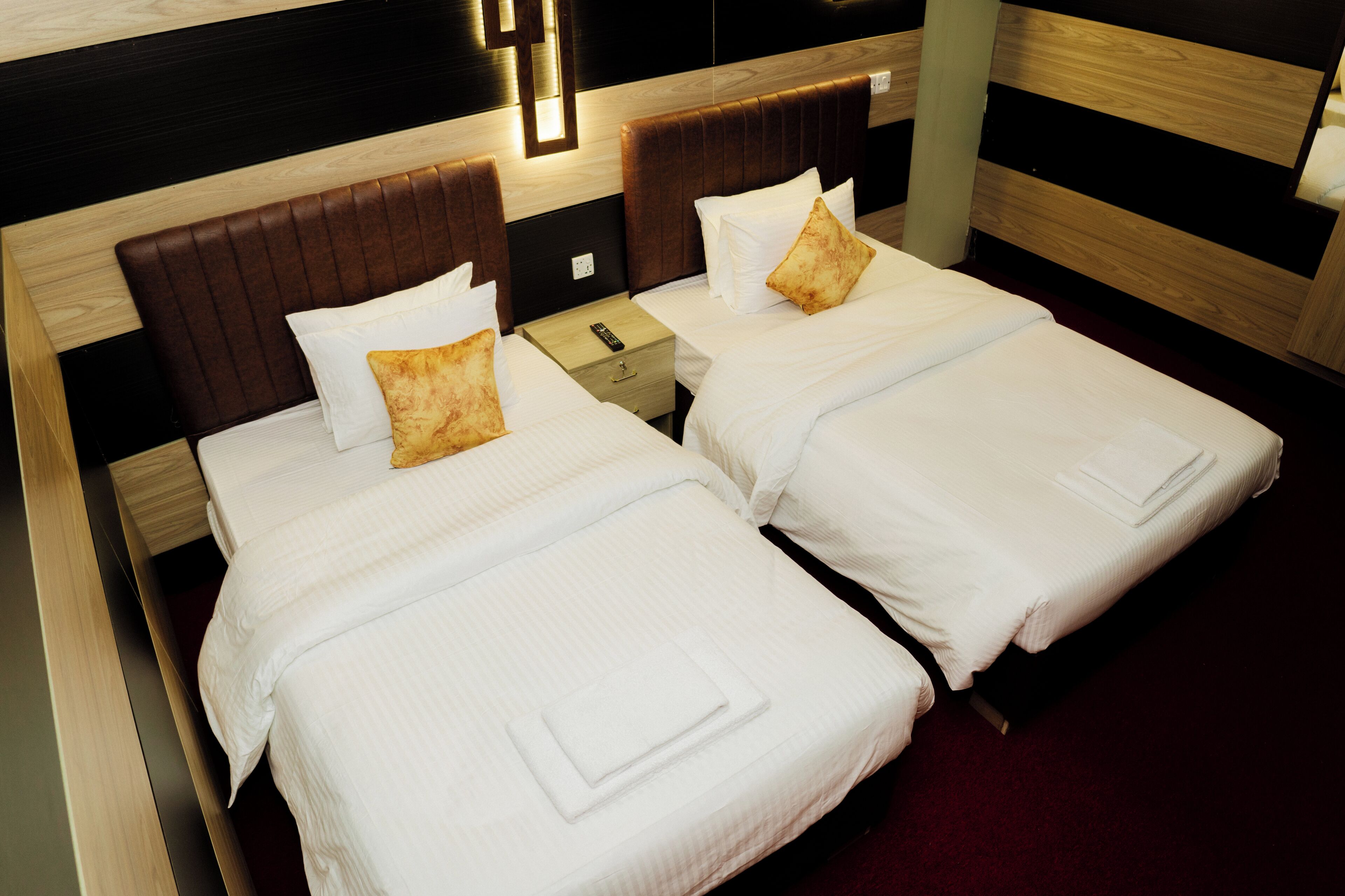 Ein Hotelzimmer mit zwei Einzelbetten, jeweils mit Kissen und Fernbedienung auf einem Nachttisch.