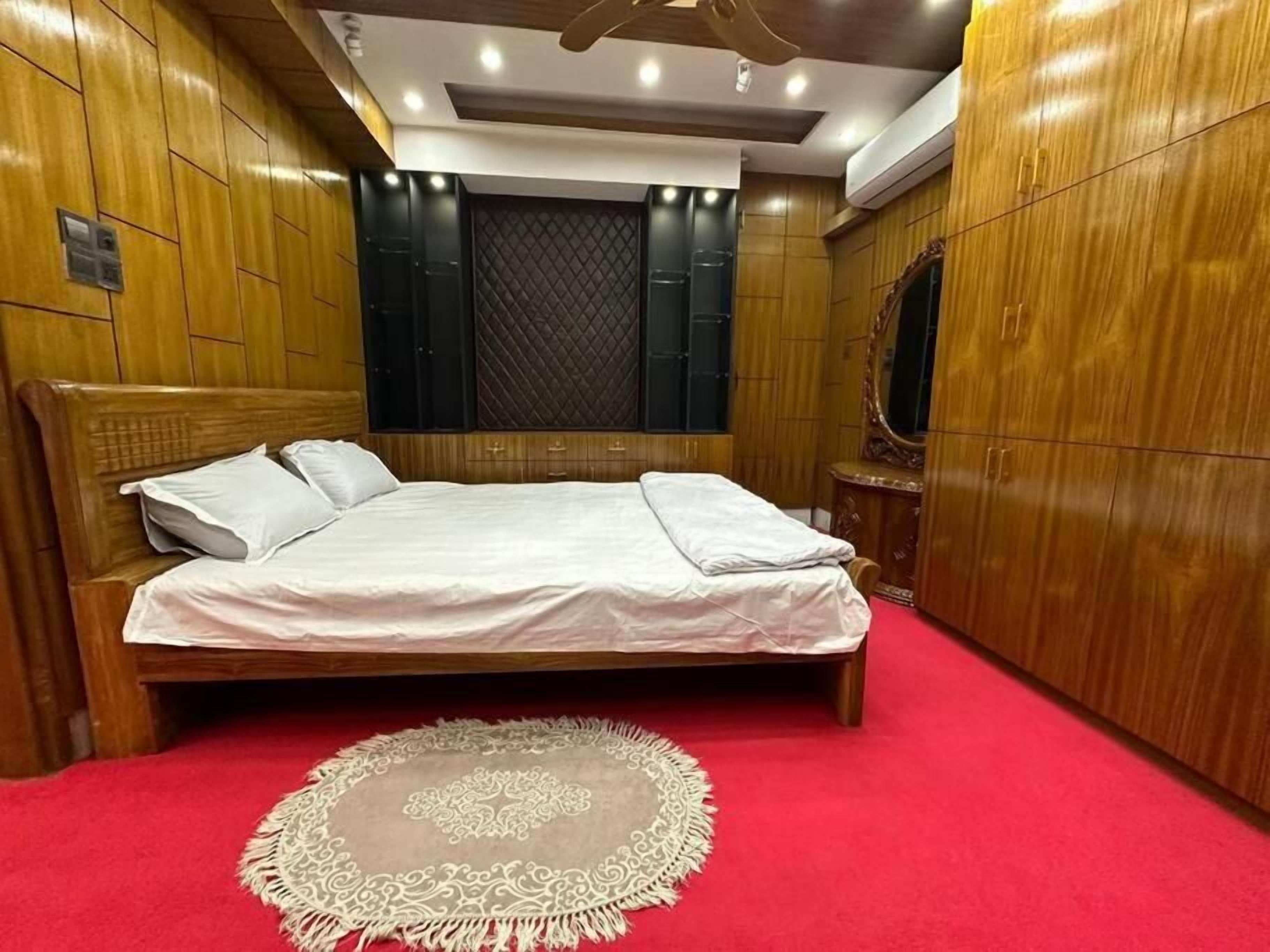 Un dormitorio ordenado con una cama grande, un armario de madera y una alfombra roja.