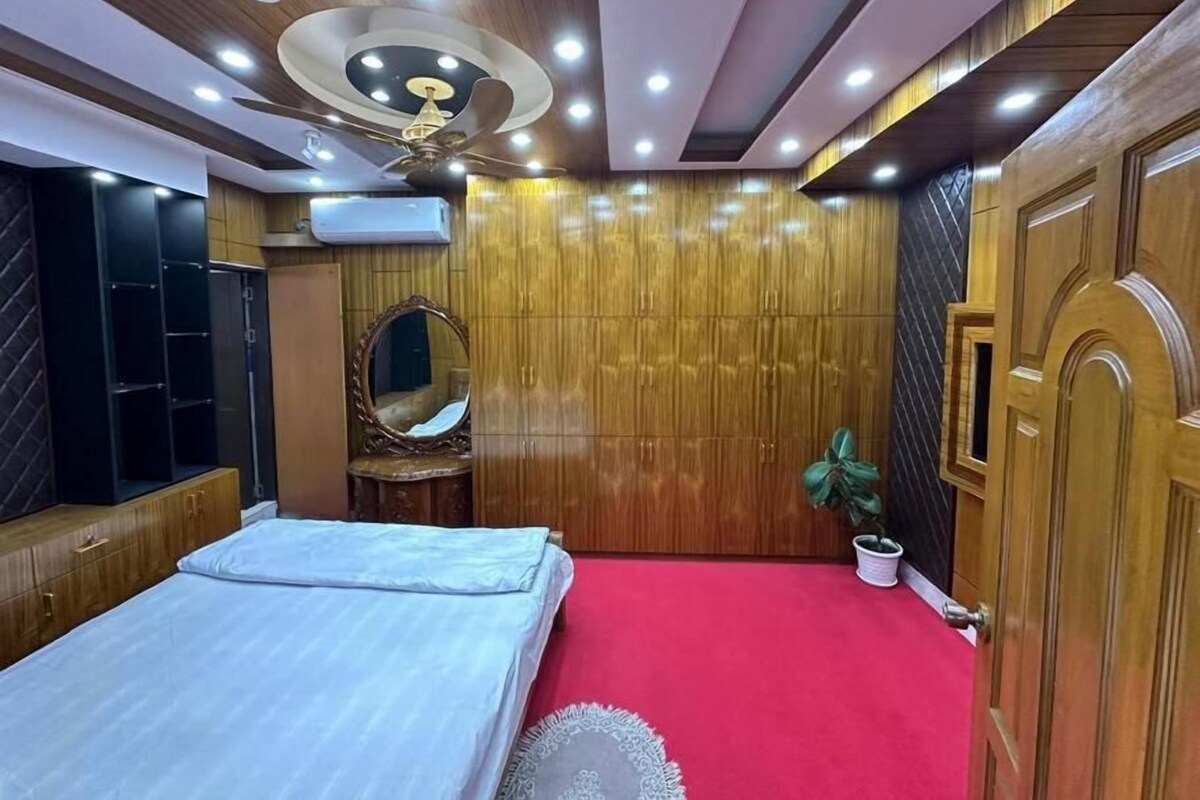 Un dormitorio con cama, armario, espejo, ventilador de techo y alfombra roja.