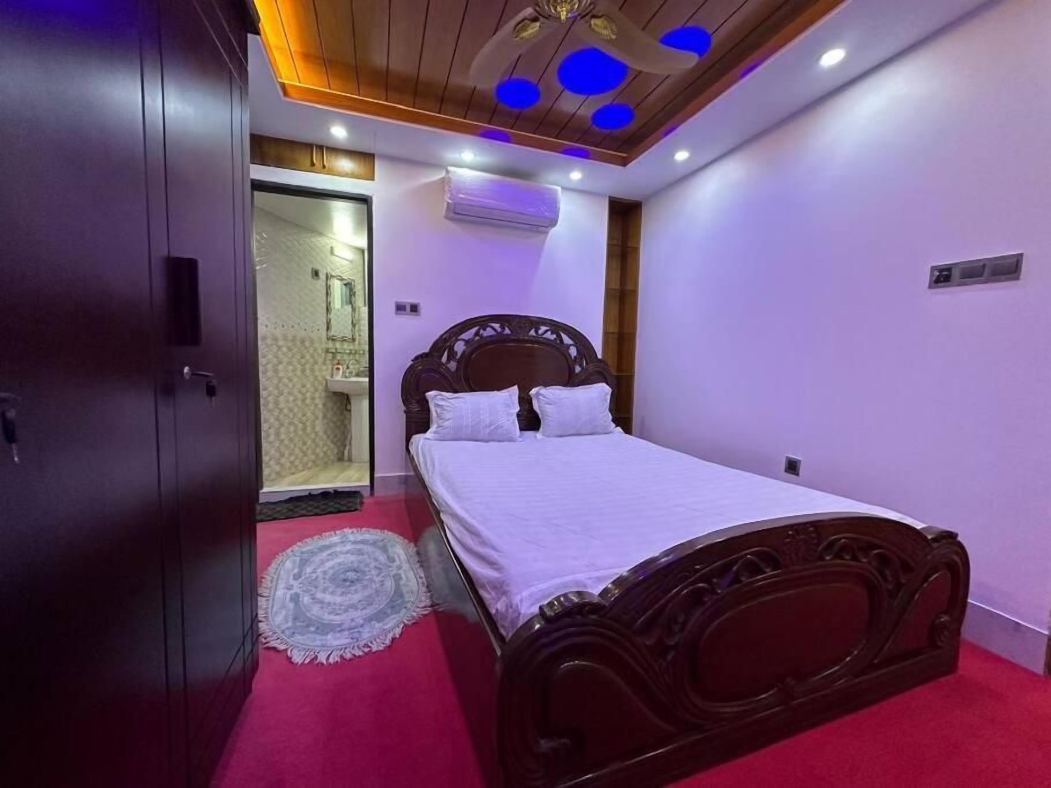 A bedroom with a wooden bed, a red carpet, and a ceiling with blue lights.