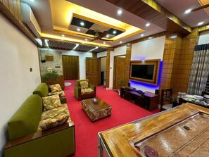 A spacious living area with a red carpet, sofas, a coffee table, a television, and a ceiling fan. - Garden view villa  (Rajshahi)