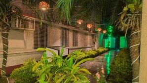 Vista nocturna de un patio con palmeras, una fuente de agua y arquitectura tradicional.
