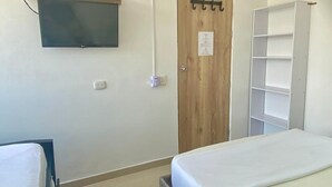 Un dormitorio con cama, televisor montado en la pared, puerta de madera y estantería blanca.