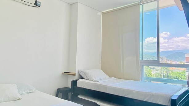 Una habitación de hotel con dos camas individuales, un ventanal con vistas a la ciudad y un ventilador de techo.
