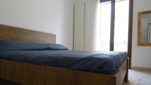 A single bed with a wooden headboard in a room with stone flooring and a window with curtains. - La Luna Guest House (Castellammare del Golfo)