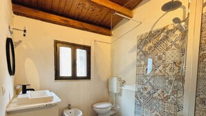 A bathroom with a wooden ceiling, a window, a toilet, a bidet, a sink, and a shower with patterned tiles. - La Luna Guest House (Castellammare del Golfo)
