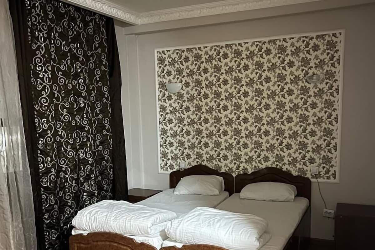 Un dormitorio con una cama de madera, dos mesitas de noche, un tapiz con motivos decorativos en la pared y una cortina con diseño de remolinos.