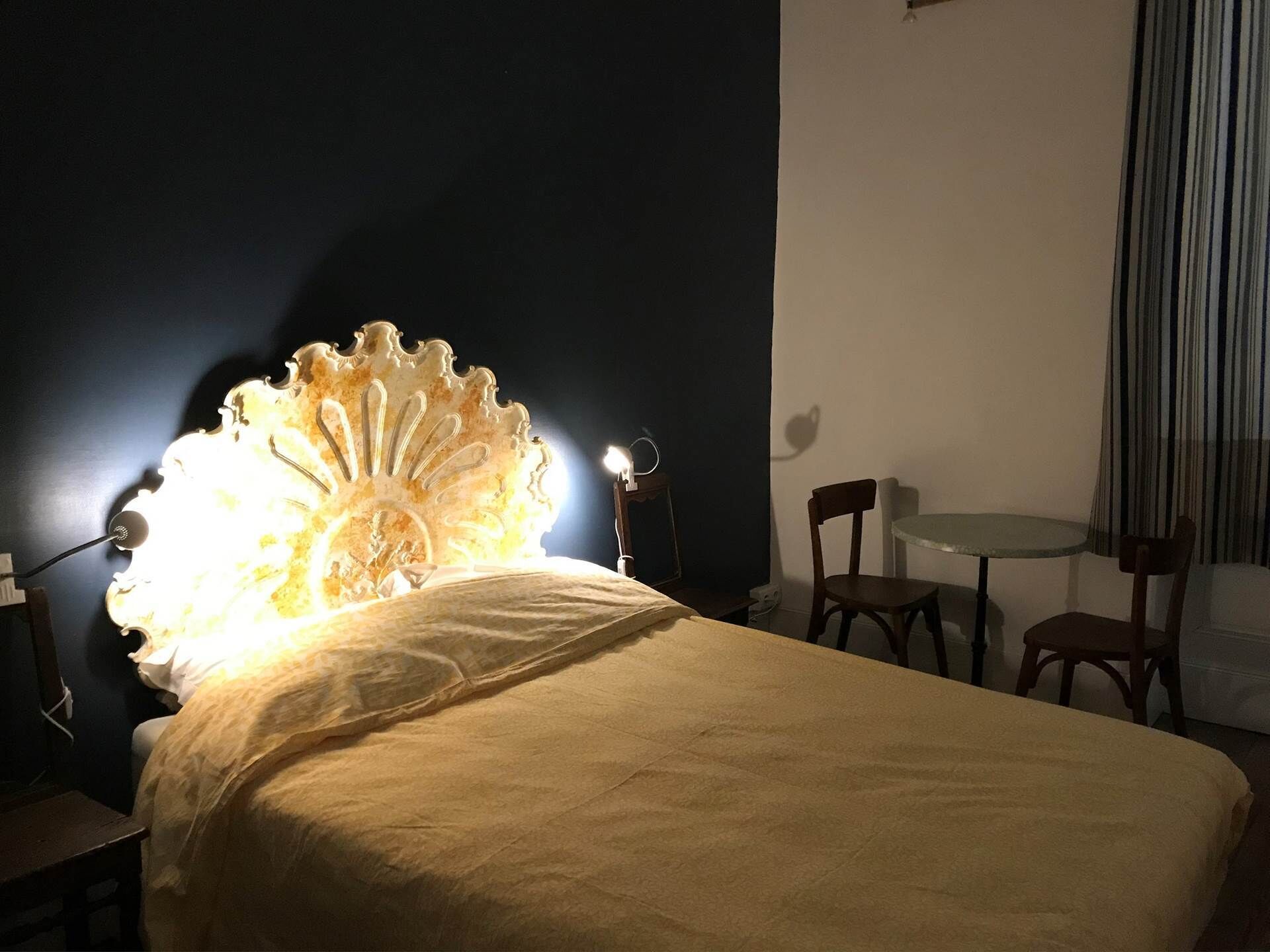 Un lit avec une tête de lit décorative, une table de chevet, une chaise et une petite table ronde avec une chaise.