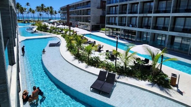 A resort pool area with multiple swimming pools, palm trees, and modern buildings. - Gav Porto Alto Resorts (Ipojuca)