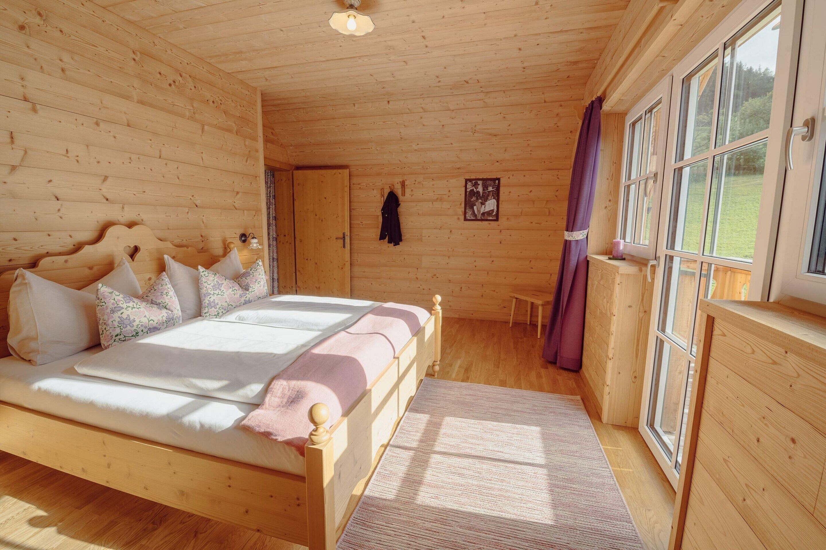 Un dormitorio de cabaña de madera con cama, ventana y puerta.