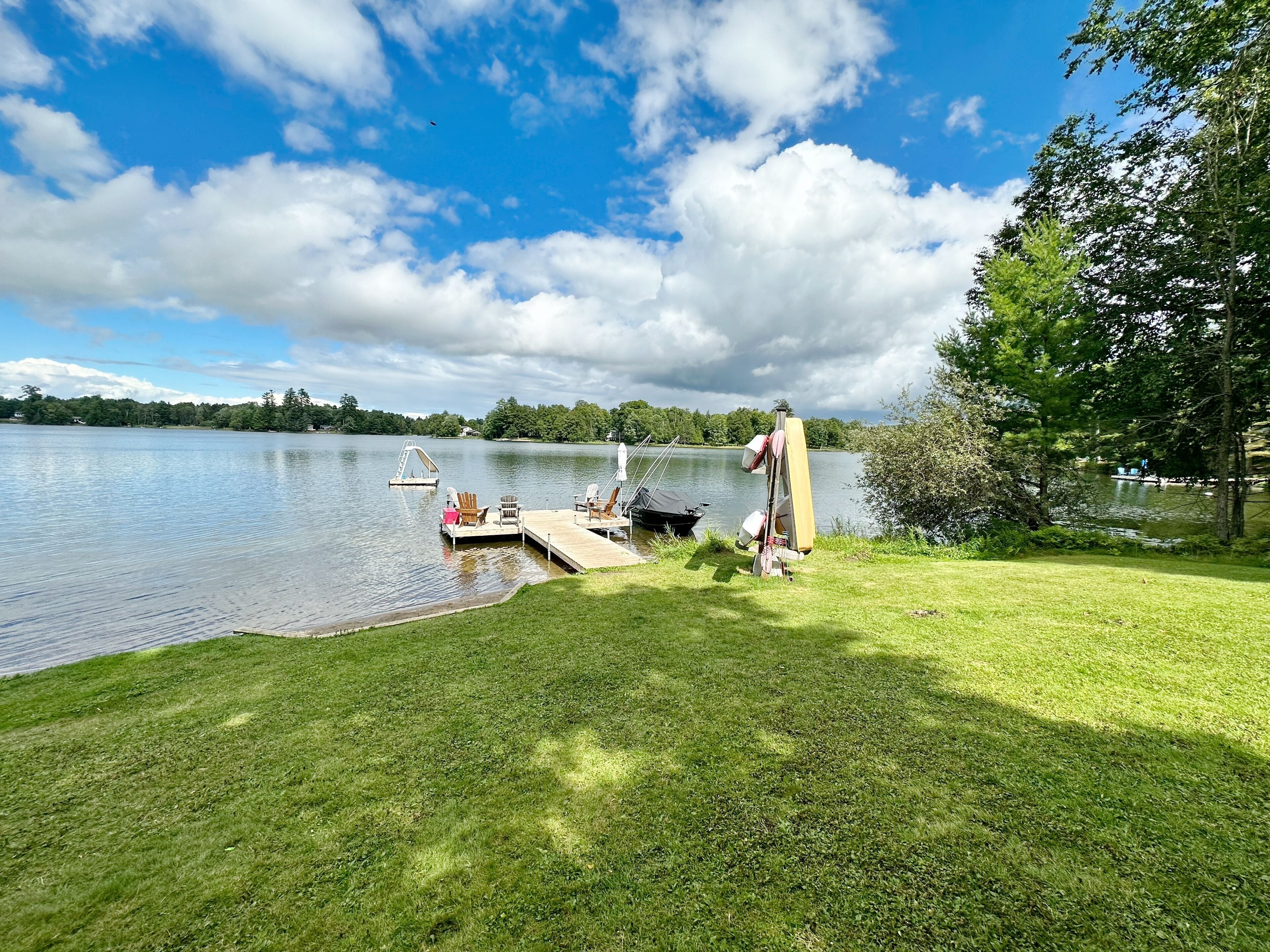 A lakeside dock with a grassy area, a small boat, and a paddleboard.