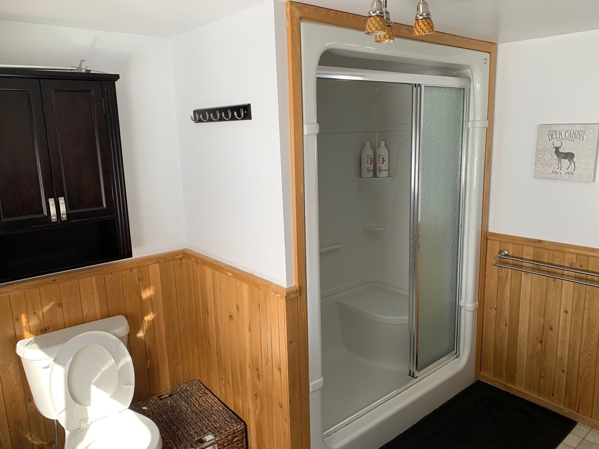 Un baño con pared de paneles de madera, inodoro blanco, cabina de ducha de vidrio y toallero.