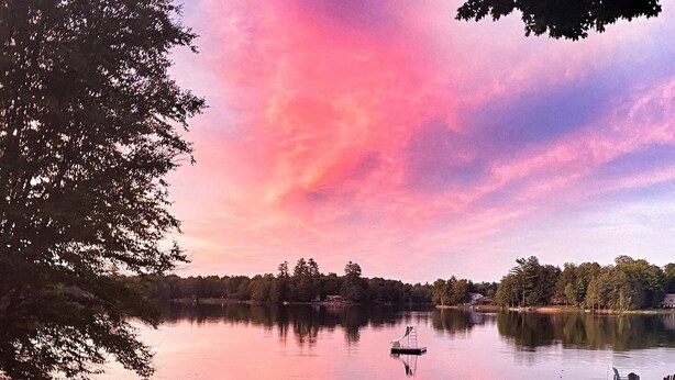 Una terraza junto al lago con sillas Adirondack rojas, un brasero y vistas al lago y árboles.