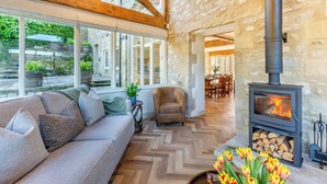 A cozy interior with a stone wall, a sofa, a fireplace, and a view through large windows.