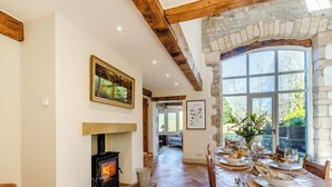 A dining area with a fireplace, wooden beams, stone walls, and a view of the outdoors.