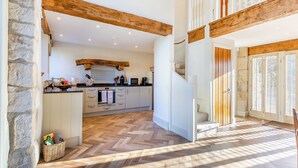 A spacious kitchen with stone walls, wooden beams, and a herringbone floor pattern.