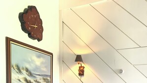 Una habitación acogedora con un sofá de madera, un cuadro enmarco, un reloj de pared y una lámpara de pared.