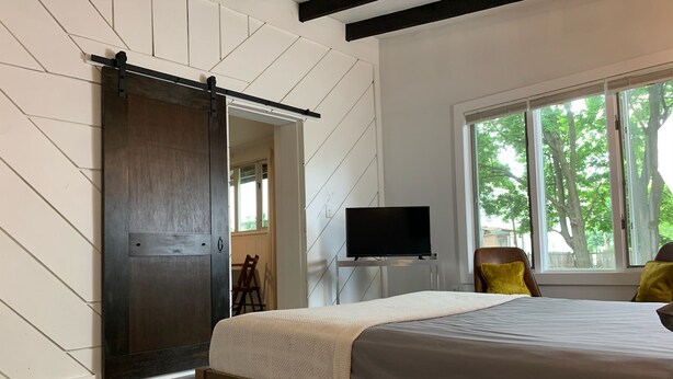 Un dormitorio con cama, televisión, ventana con vistas a árboles y puerta corredera.