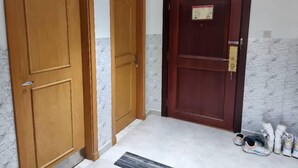 A hallway with three wooden doors, a marble wall, and a tiled floor. - Unique Hostel Dubai (Dubai)