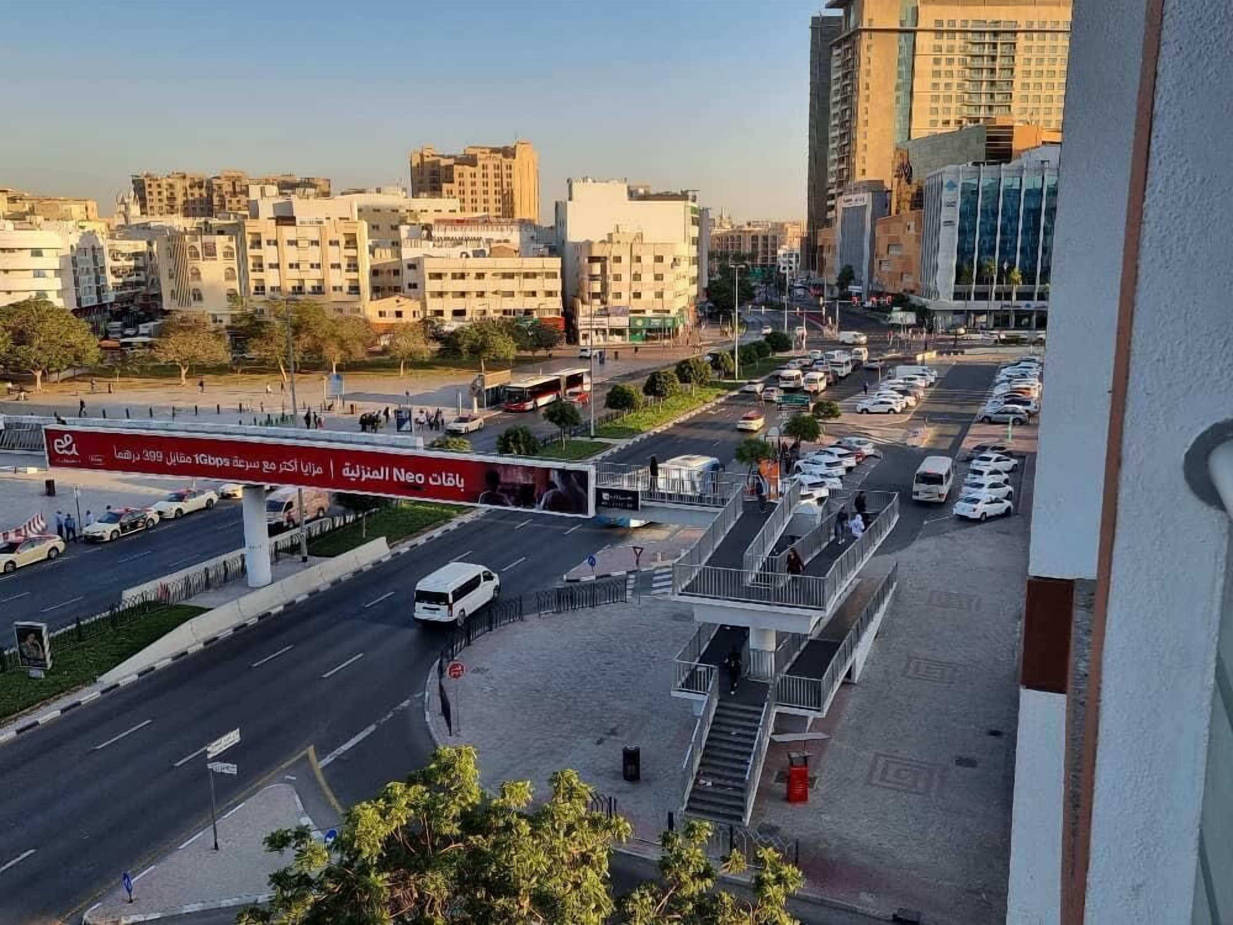 A city street with a pedestrian overpass, buildings, and parked cars.