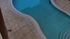 A rooftop swimming pool with a curved design, surrounded by a tiled deck and a low wall. - Unique Hostel Dubai (Dubai)