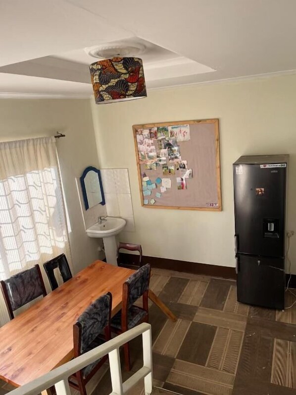 A dining area with a wooden table, chairs, a bulletin board, a sink, and a refrigerator.
