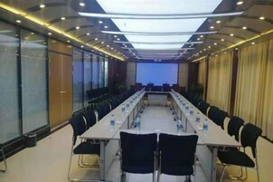 Un salón de conferencias con una larga mesa, sillas, botellas de agua y una pantalla de proyección.