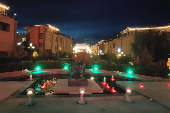 Vista nocturna de un patio central con una fuente, rodeado de edificios con ventanas iluminadas.