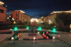 A nighttime view of a courtyard with a central fountain, surrounded by buildings with illuminated windows. - Shenghua Culture International Hotel (Linze)