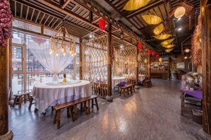 A restaurant interior with round tables, wooden benches, and a high ceiling with hanging lights.