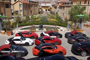 Un parking où sont garées plusieurs voitures de luxe, avec une fontaine et des bâtiments en arrière-plan.