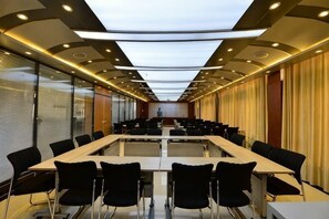 Une salle de conférence avec une longue table, des chaises noires et une cloison en verre.