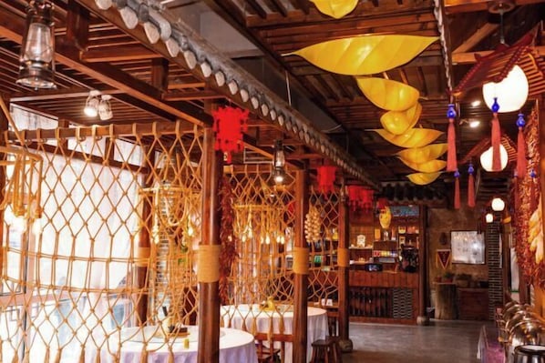A restaurant with a rustic wooden interior, tables with white tablecloths, and hanging yellow lanterns.